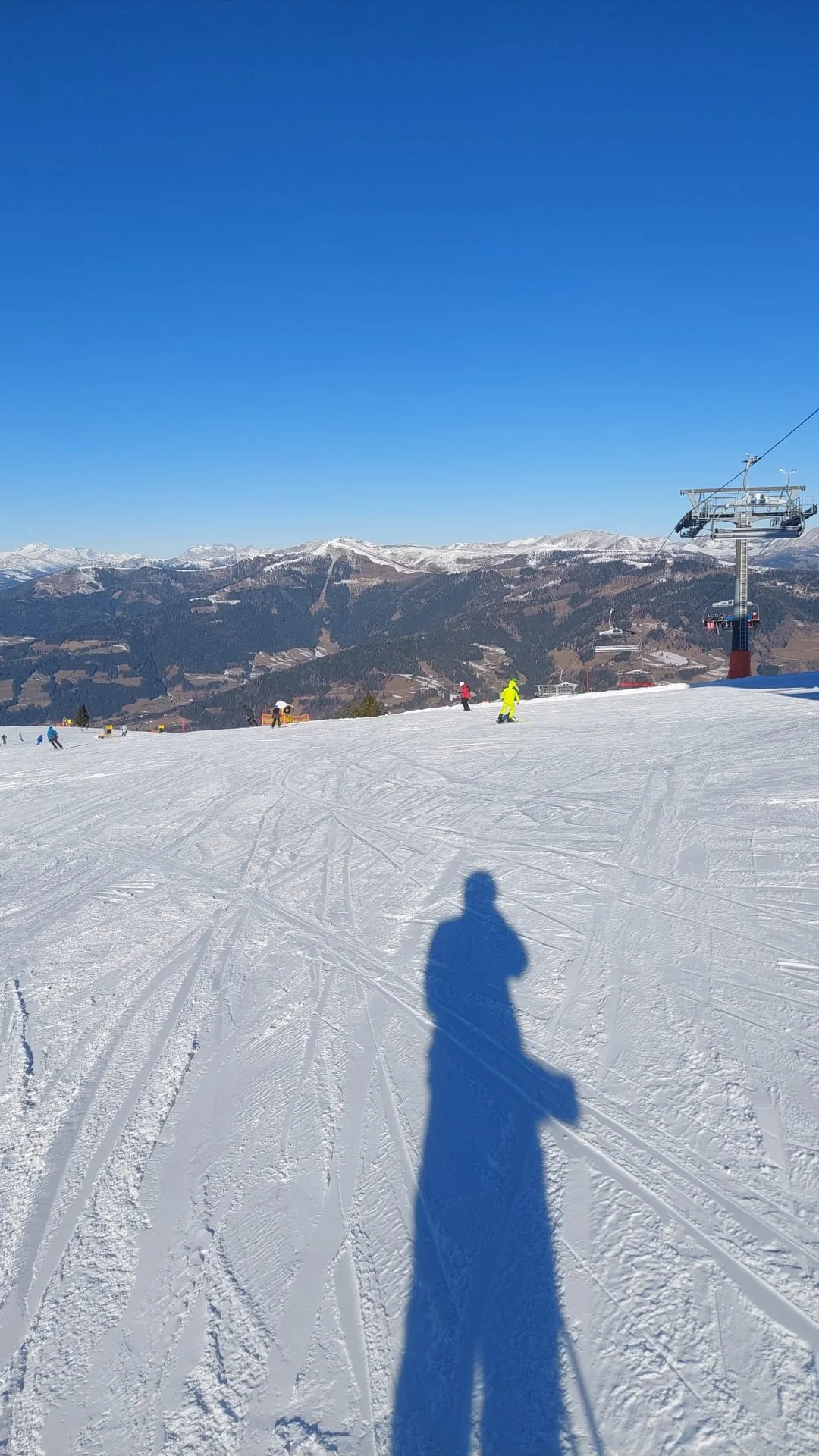 Sjena skijaša na uređenoj stazi na Gerlitzenu, u daljini skijaši, sjedežnica i planine